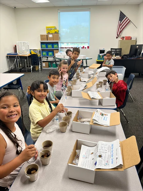 Students at a classroom table smiling as they work on their Boon-dah Box kits
